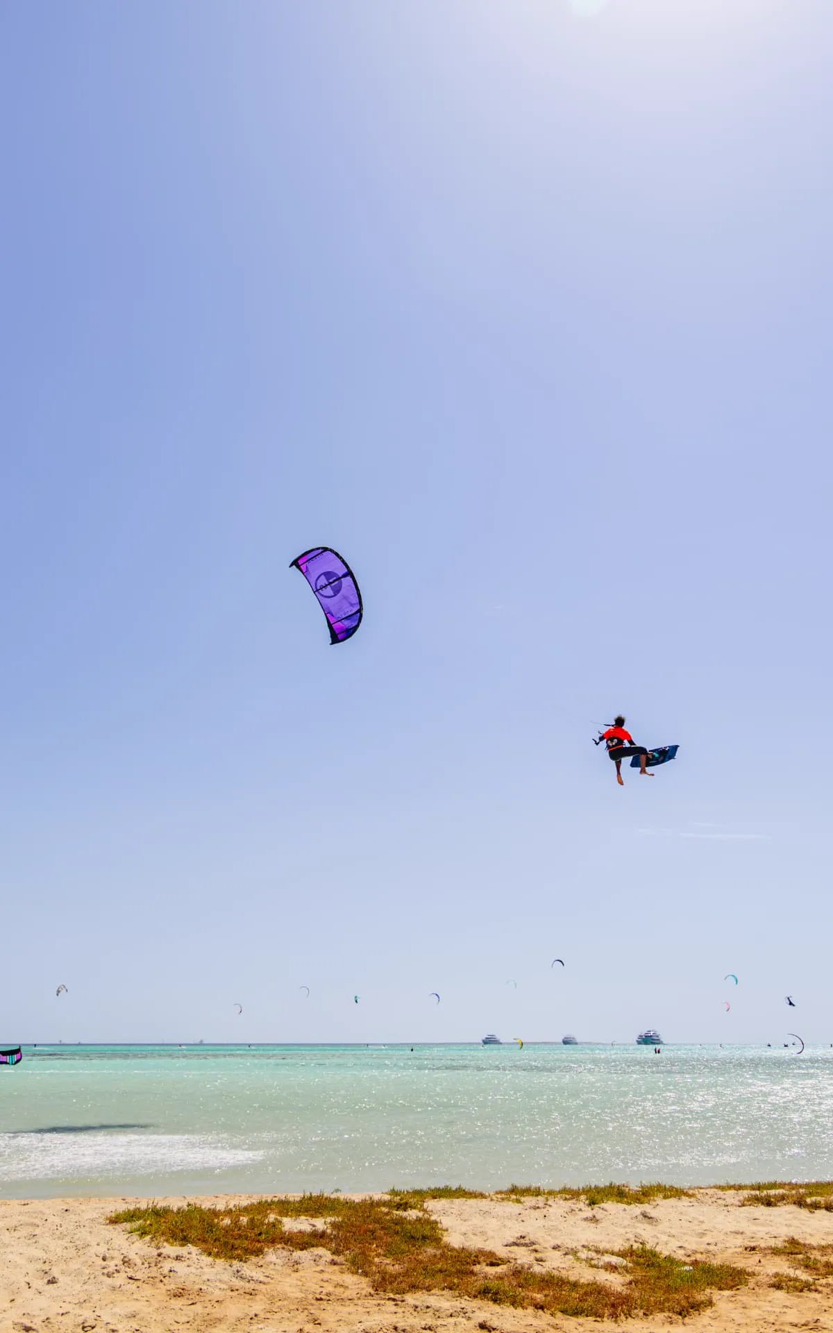 Kitesurfer in a red shirt sending a high jump under a purple kite off a sandy shoreline