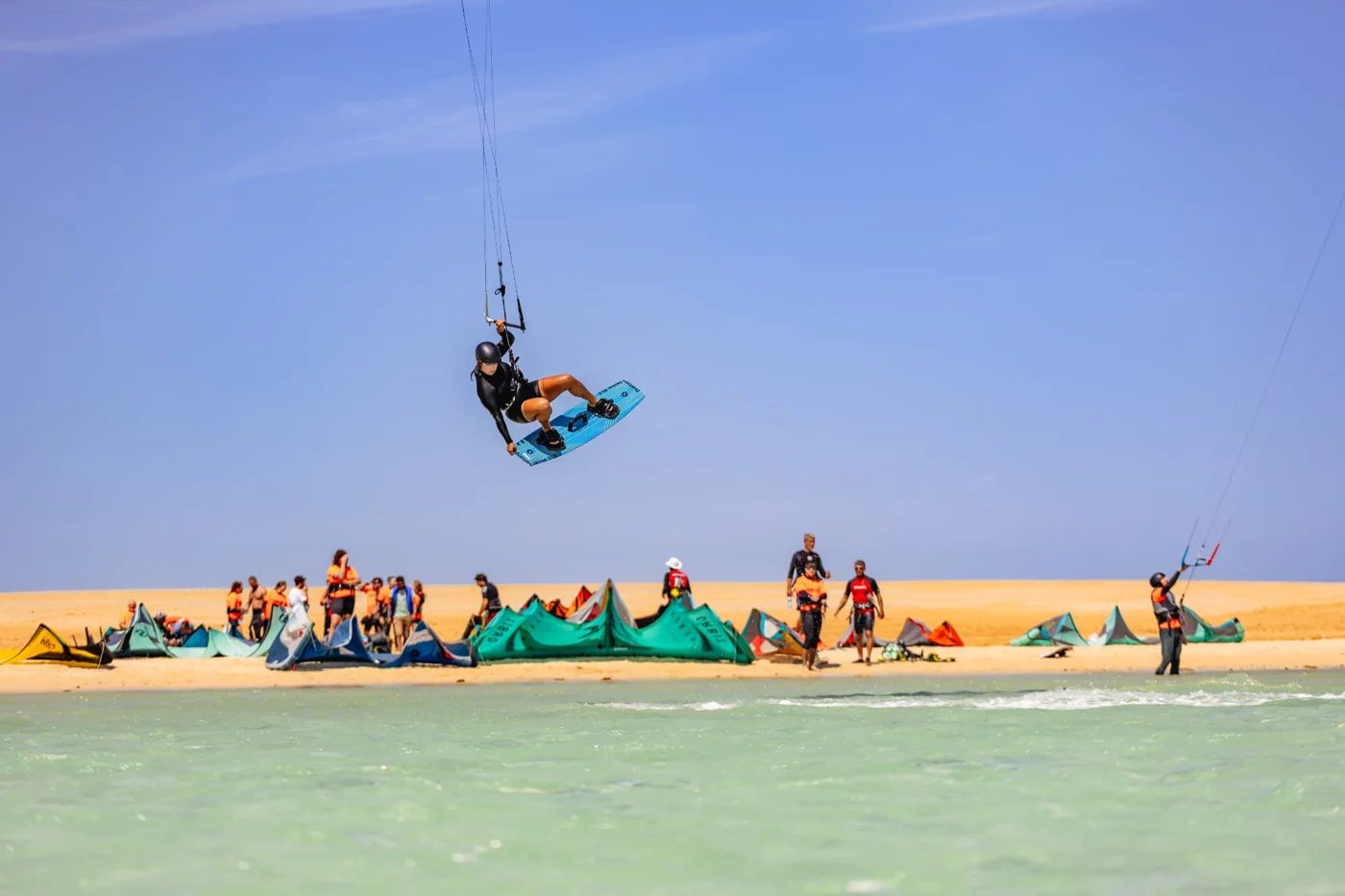 Kitesurfer jumping above the lagoon with safari guests and kites on the beach