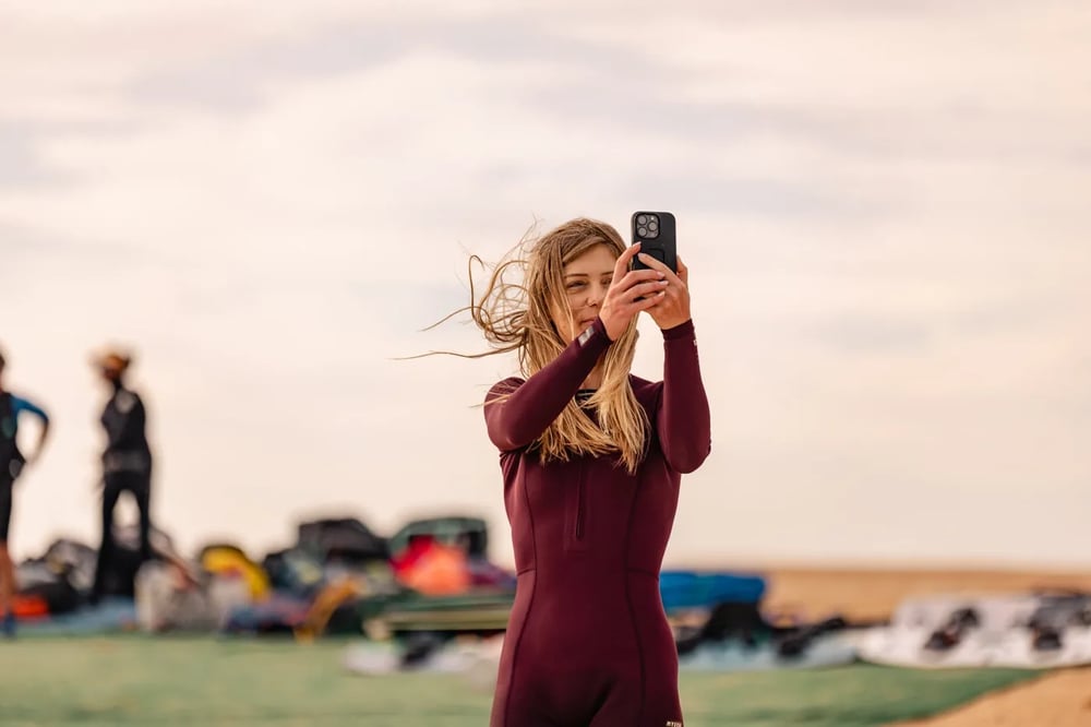Camper taking a photo with her phone on the beach at the camp