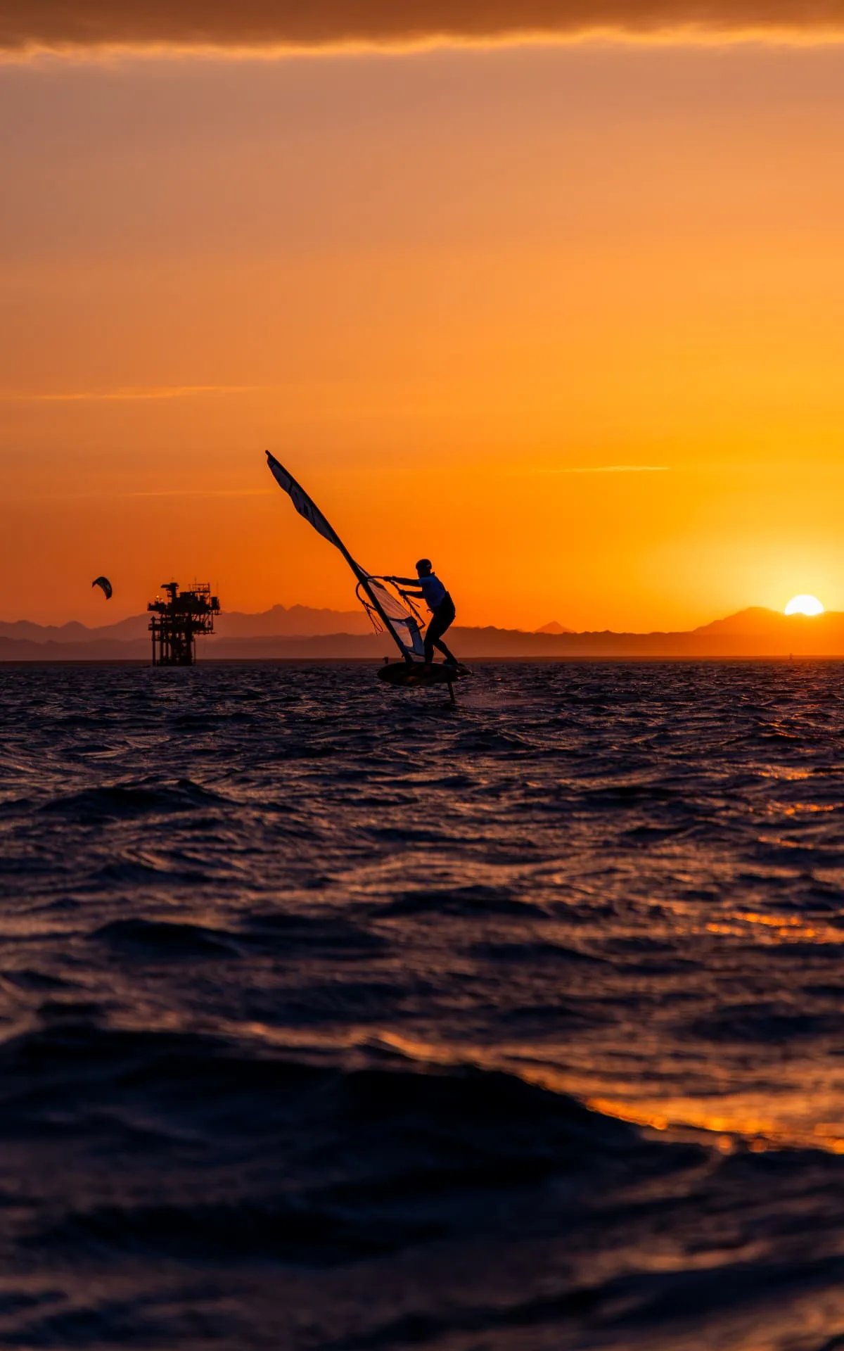 Windfoiler gliding above the water against a Red Sea sunset