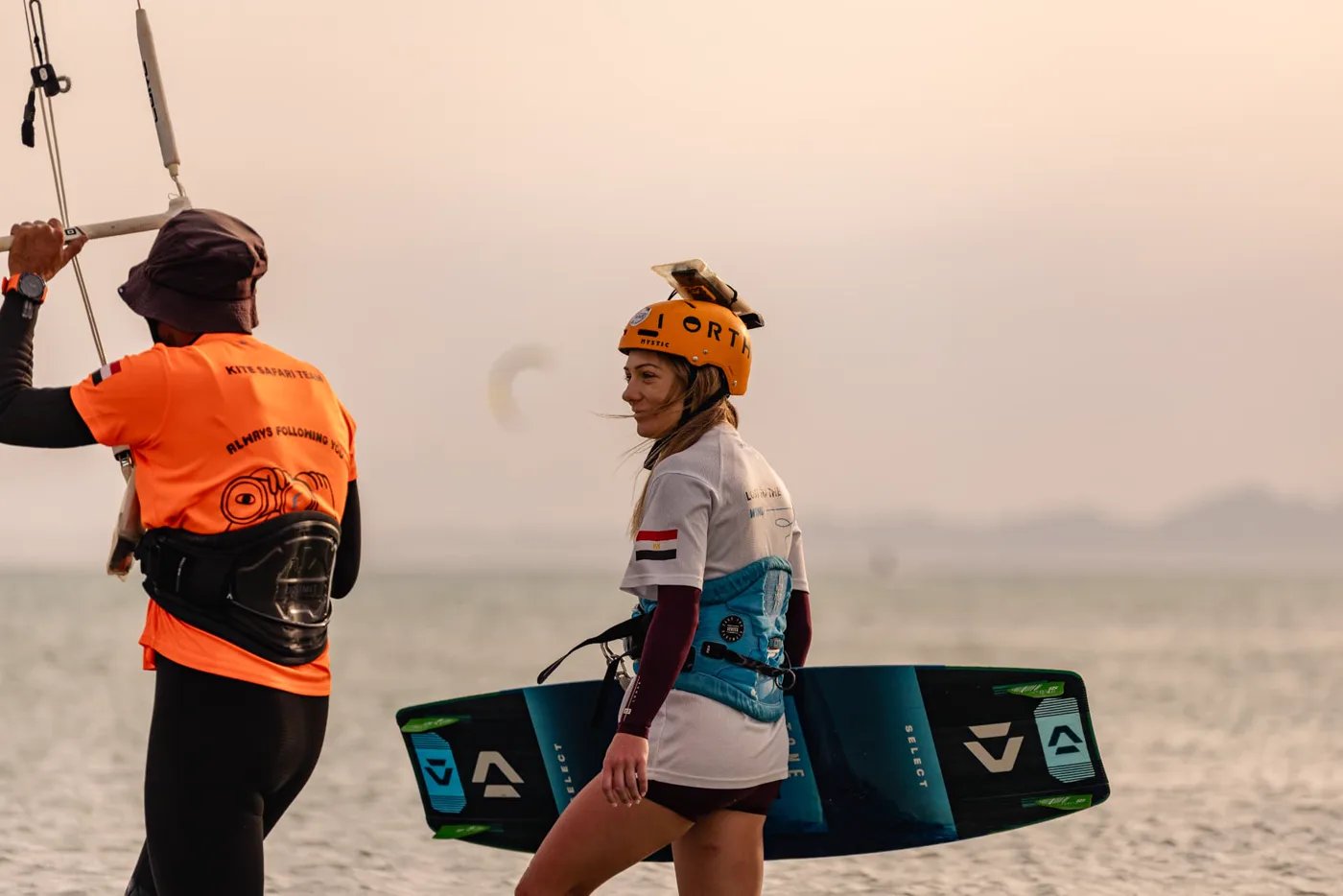 Student carrying her board through the shallows as the instructor holds the control bar