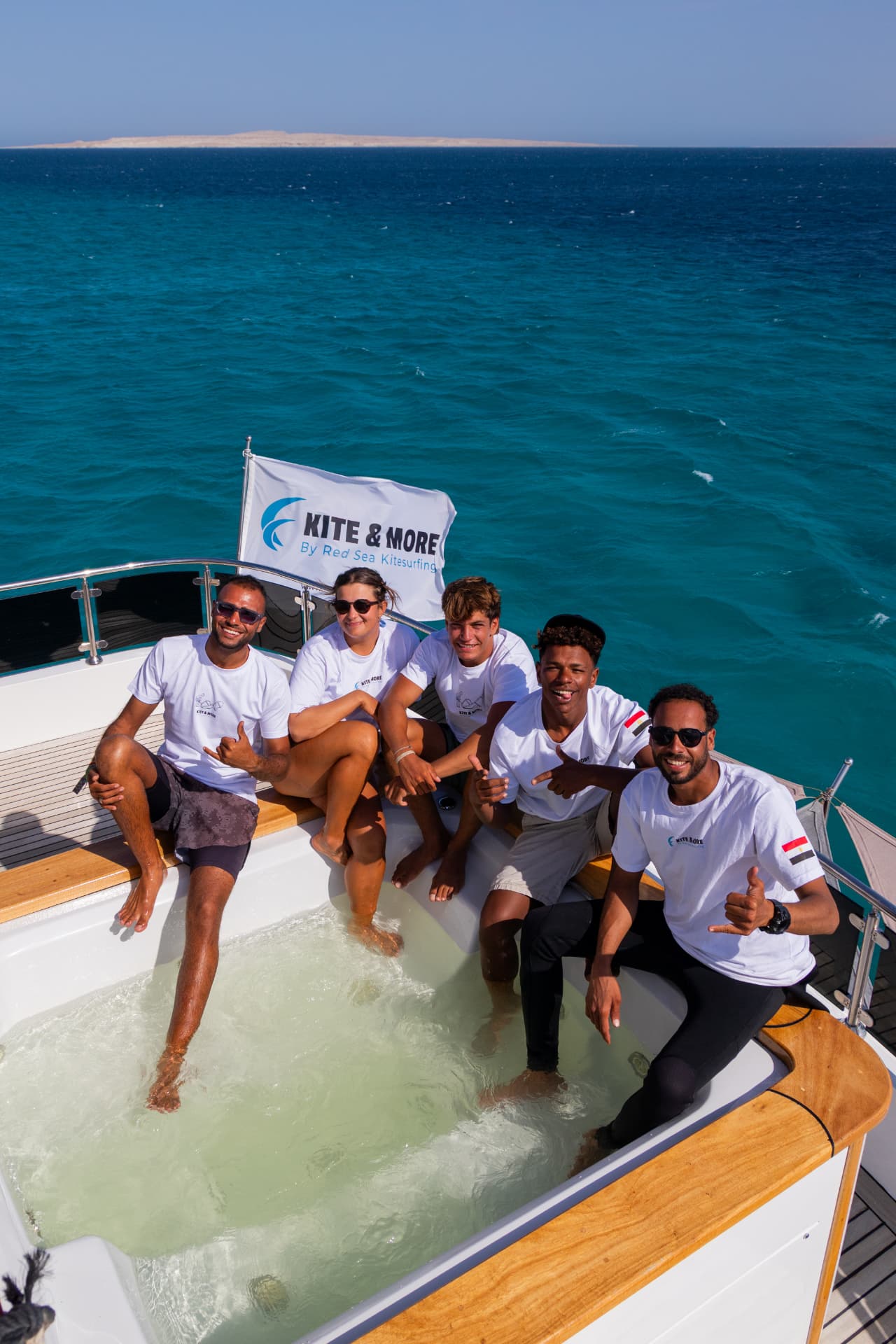 The same five crew members sitting around the hot tub on the boat's rear deck with their feet in the water