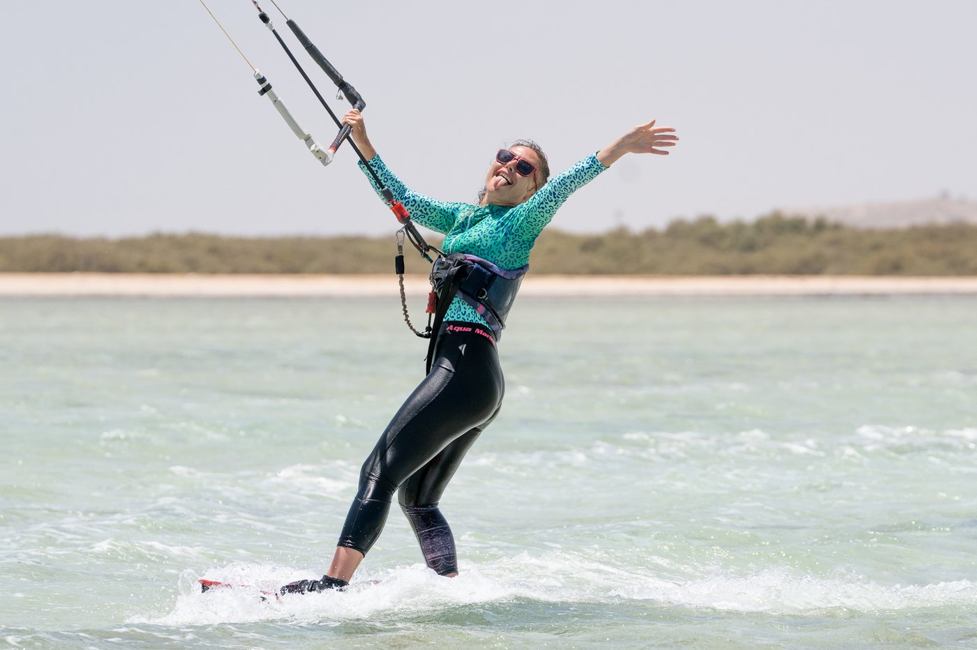Joyful kitesurfer riding across a turquoise Red Sea lagoon with arms wide open