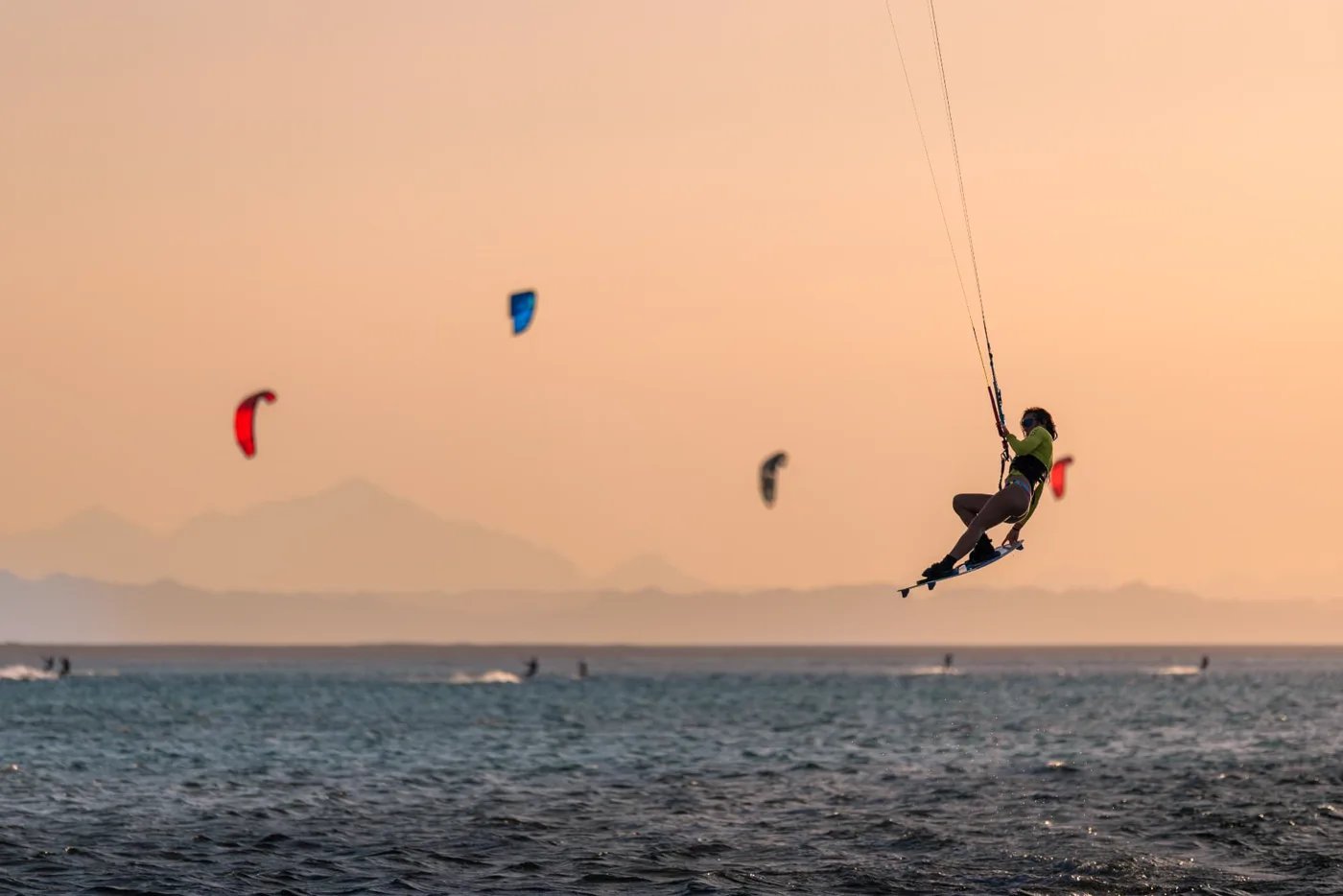 Kitesurfer hanging high above the water against a hazy sky with distant mountains behind