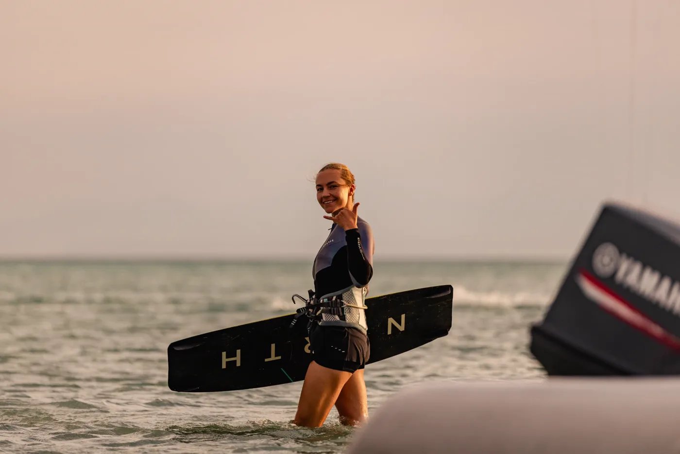 Smiling guest standing in shallow water with her board under her arm beside the boat