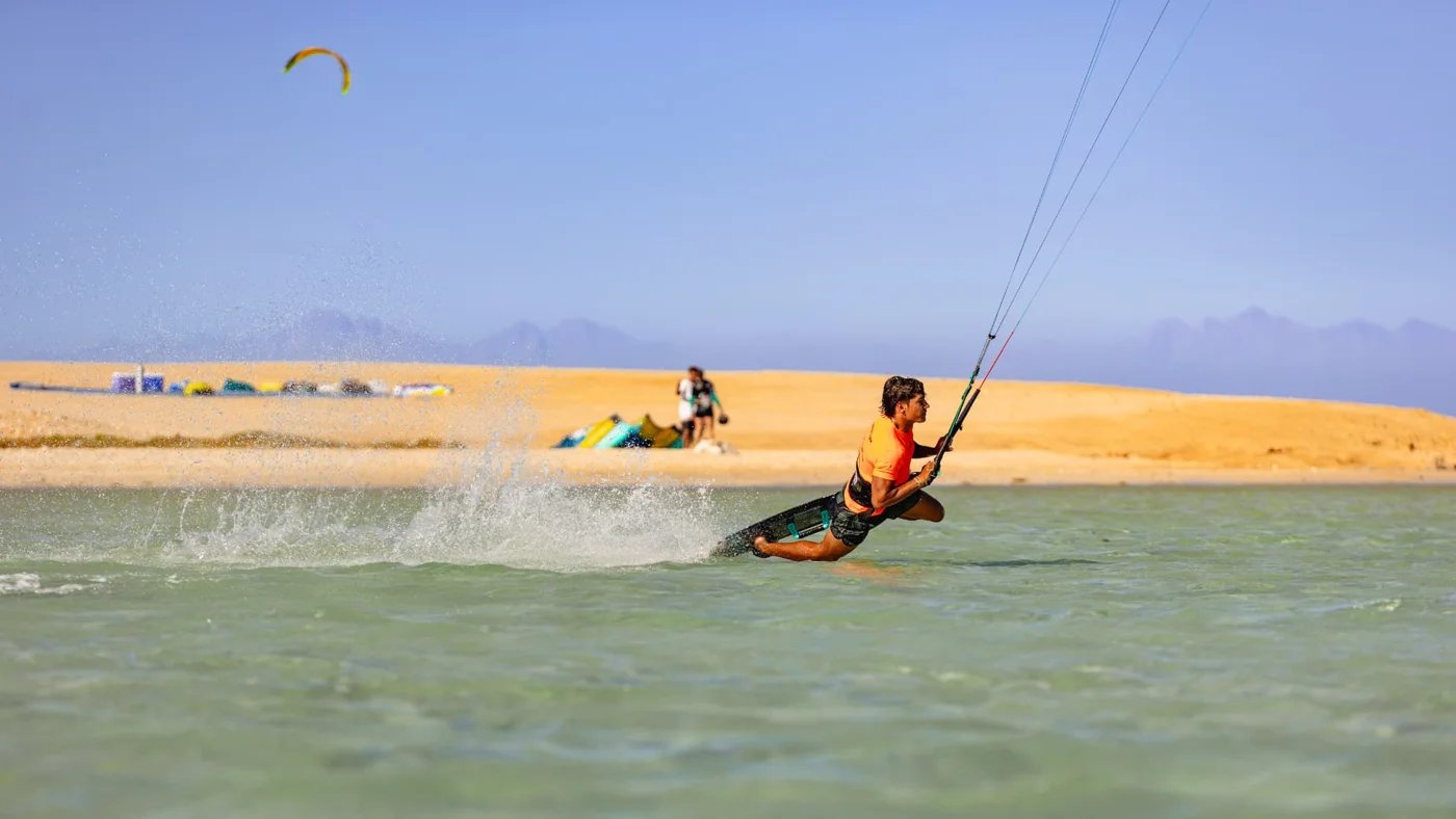 Kitesurfer carving across a Red Sea lagoon beside a sandy island