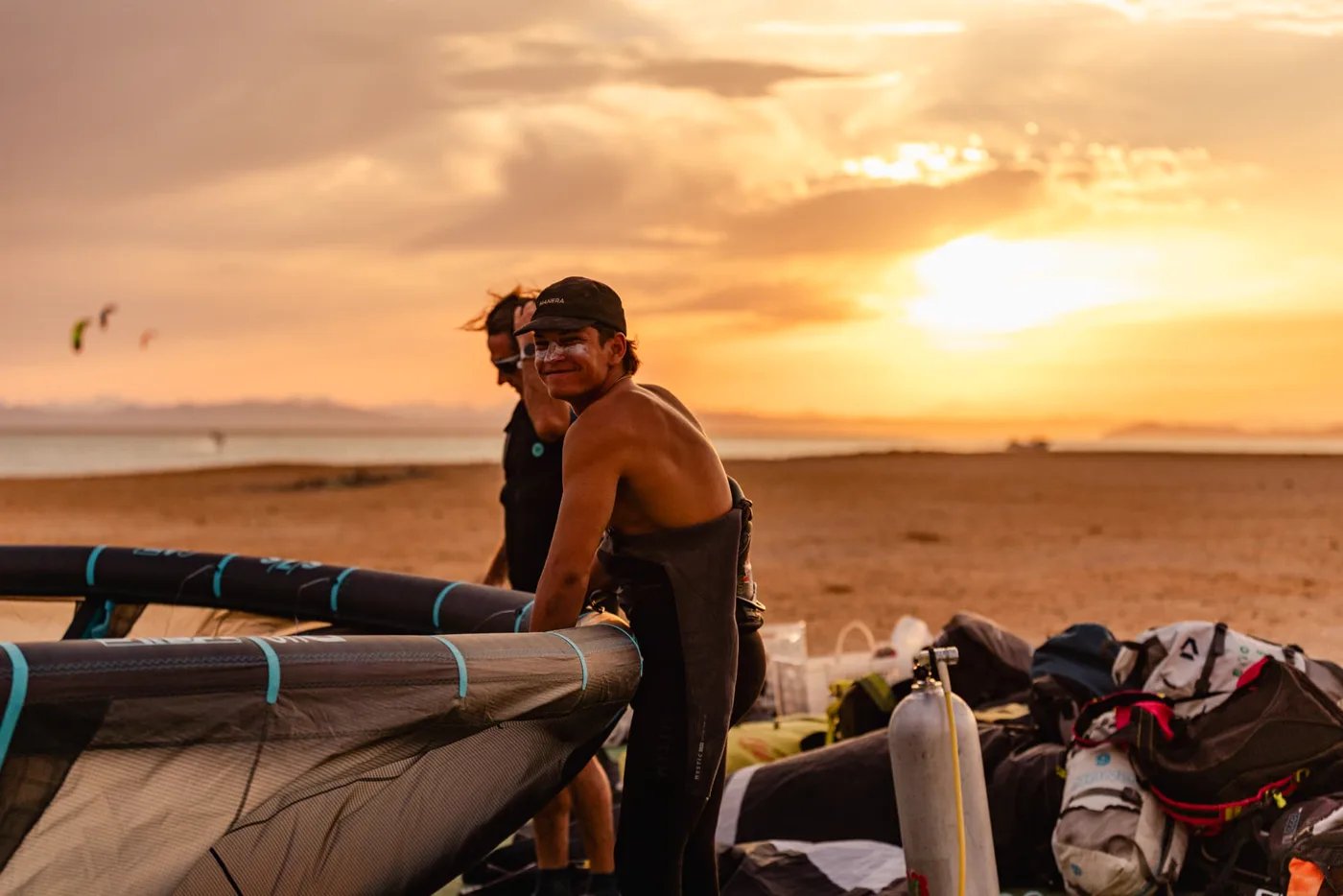 Guest in a cap and wetsuit rigging his kite gear on the beach at sunset