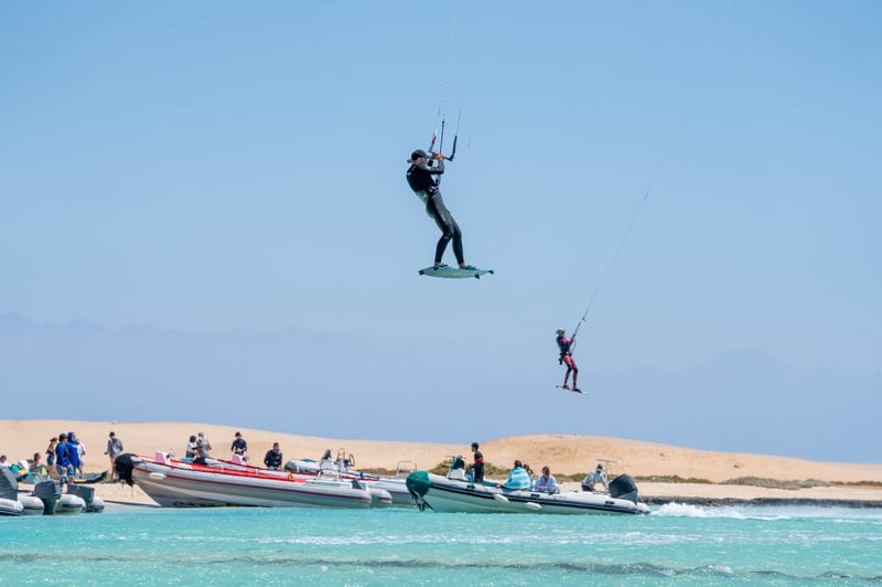 Kitesurfer boosting high above turquoise water near support boats