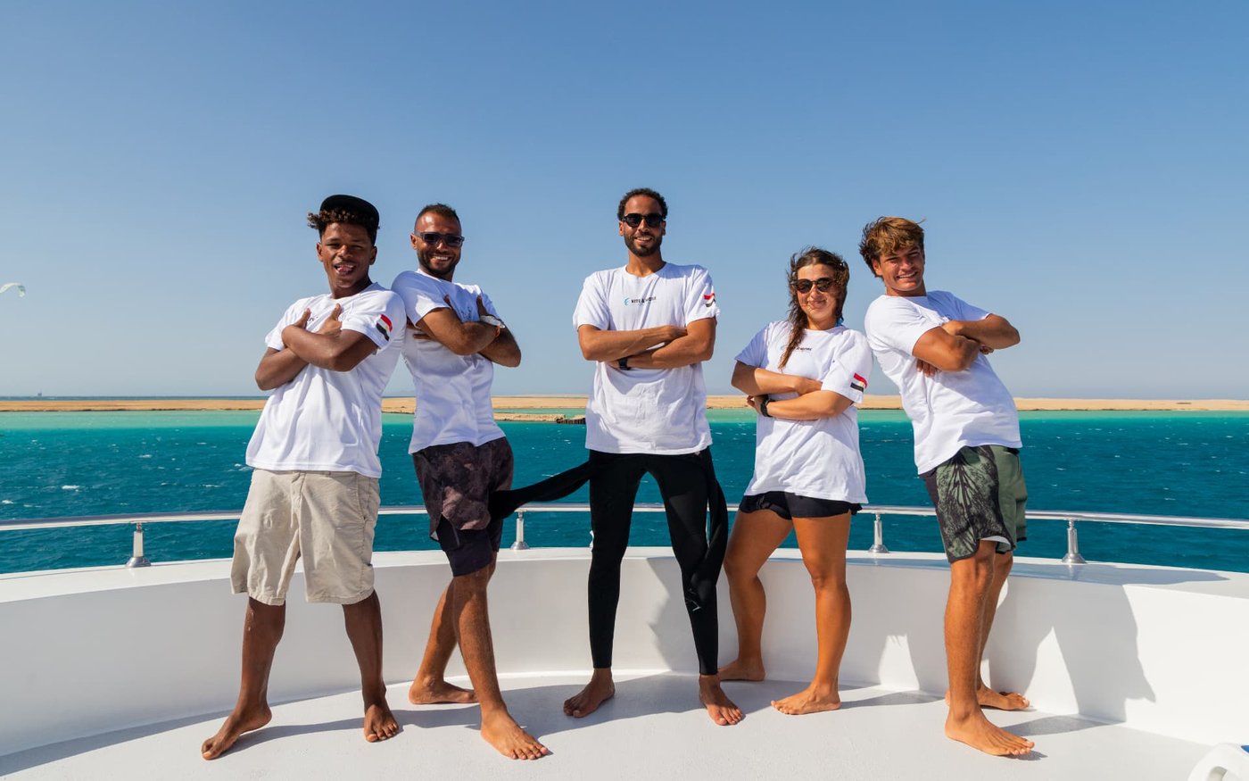 Five Kite & More crew members in white shirts standing arm-in-arm on the sun deck of the safari boat