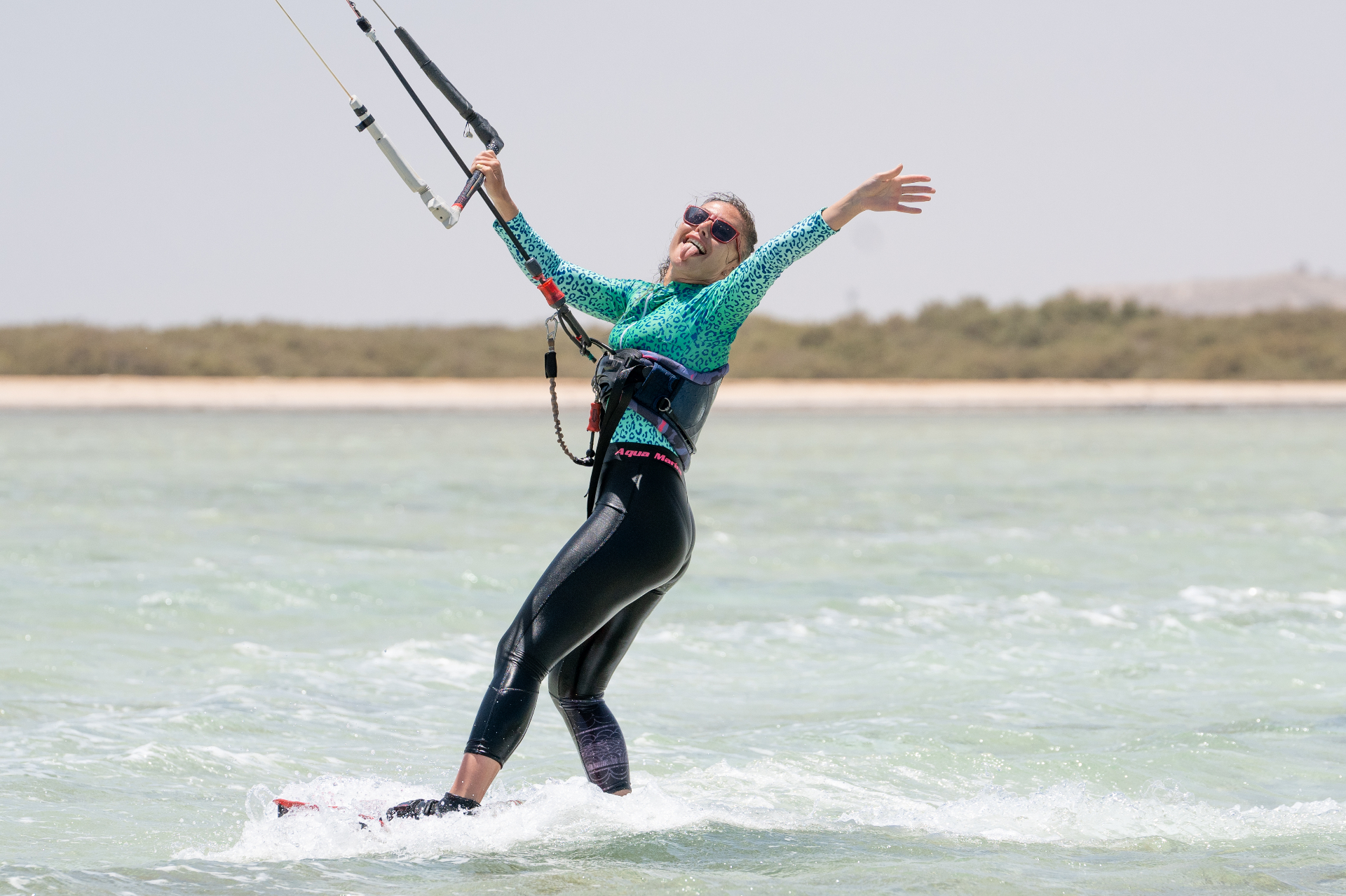 Joyful kitesurfer riding across a turquoise Red Sea lagoon with arms wide open