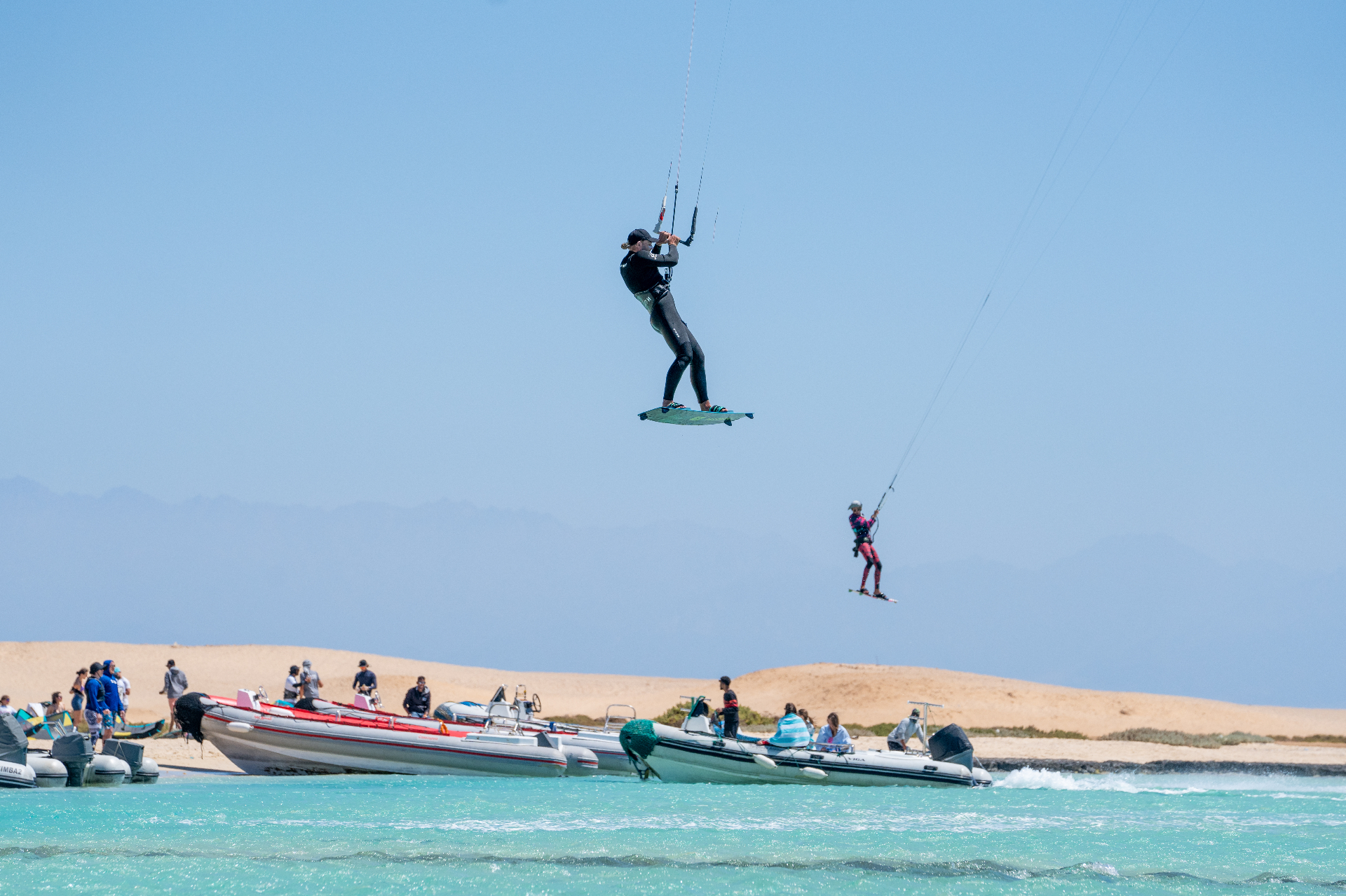 Kitesurfer boosting high above turquoise water near support boats