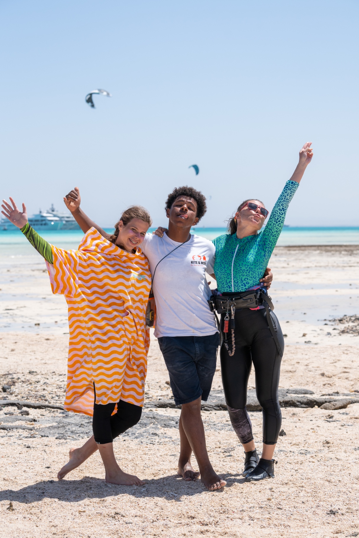 Three friends celebrating with arms in the air on the beach