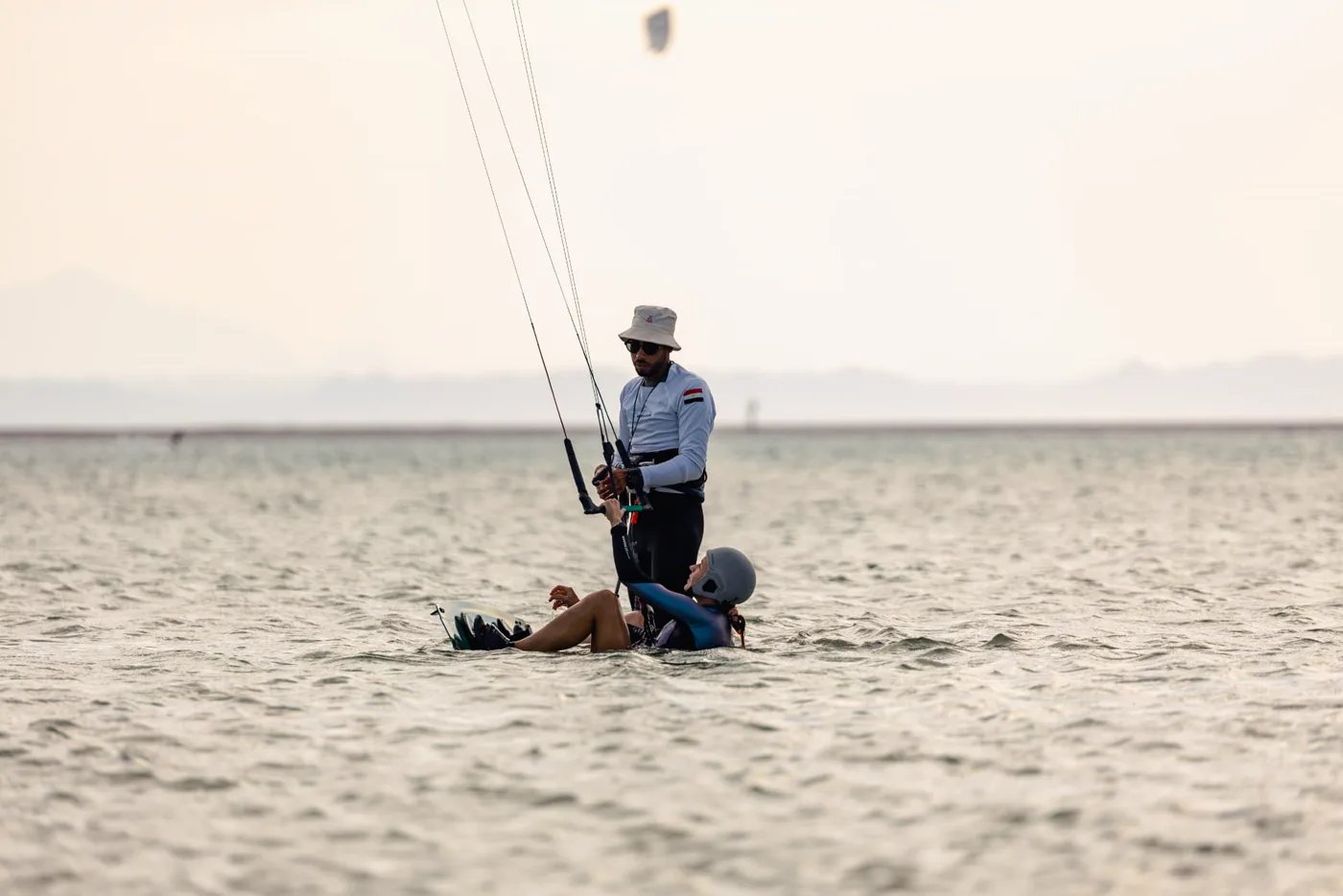 Instructor helping a seated student with her board in shallow water during a lesson